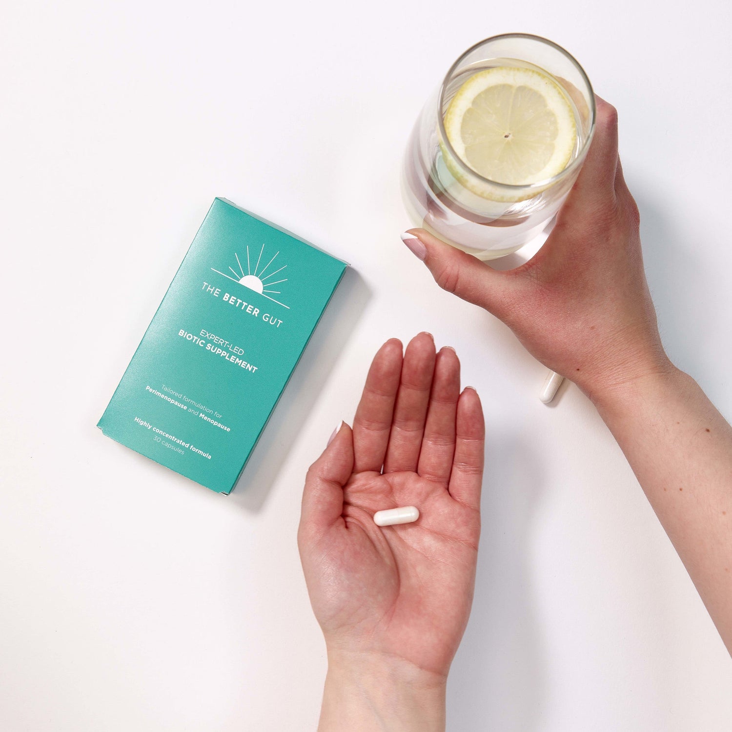 The Better Gut supplement package, hand holding a pill and other hand holding a glass of water with a slice of lemon.