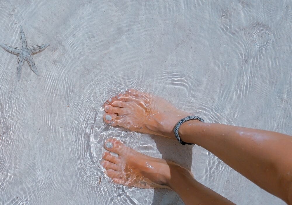 A woman's feet in shallow water on a beach next to a starfish