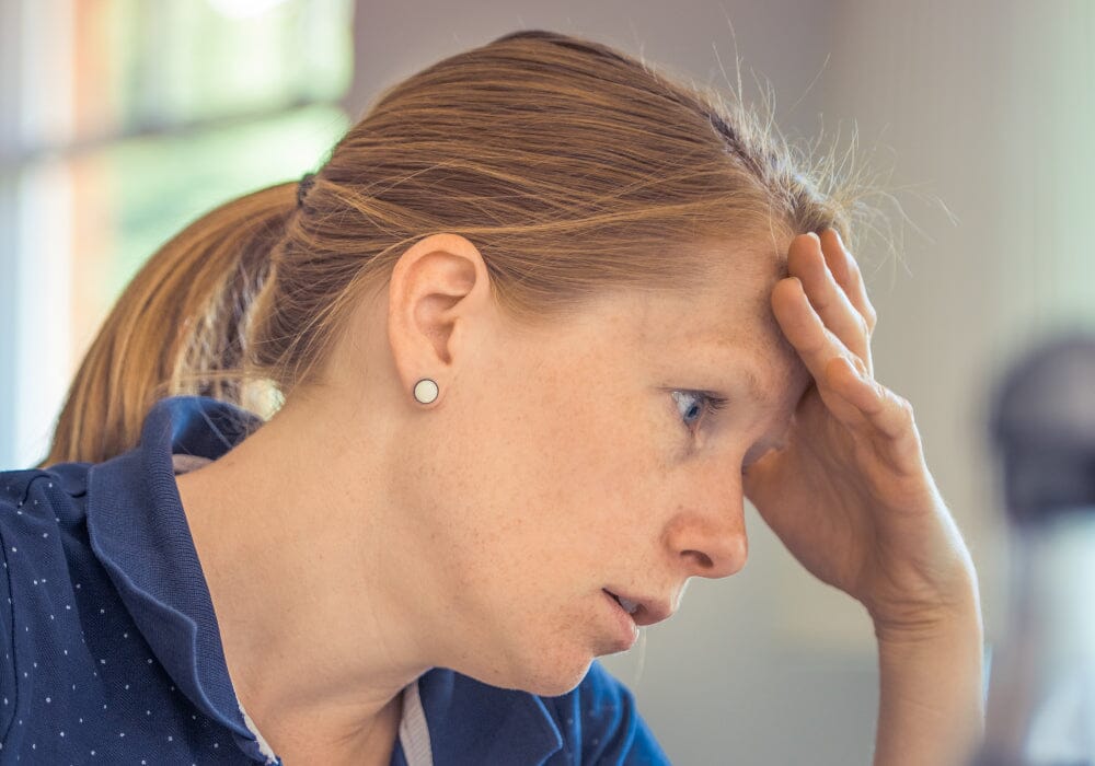 A headshot of a woman with her hand to her forehead looking stressed