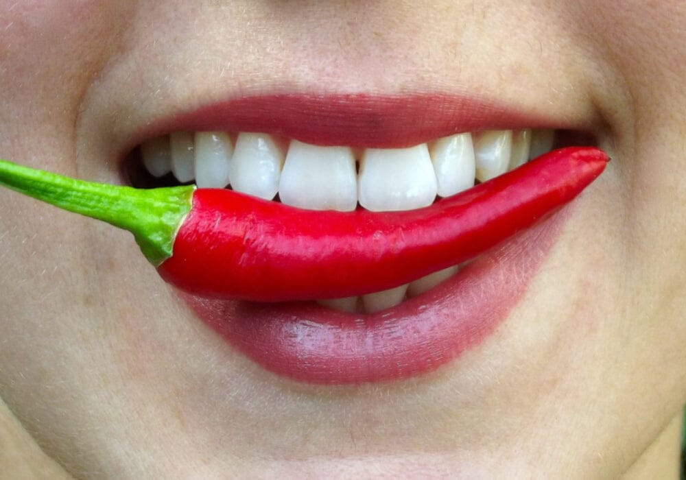 A close up of a woman's mouth biting a red chilli pepper