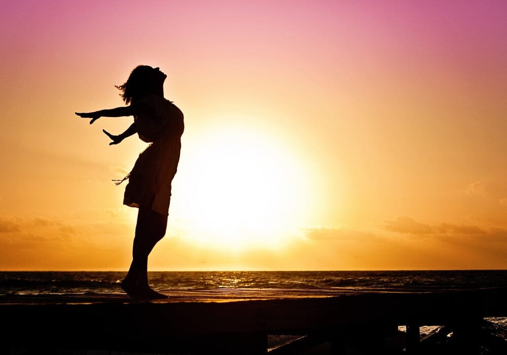 A woman in a dynamic pose silhouetted against the sun setting over the sea