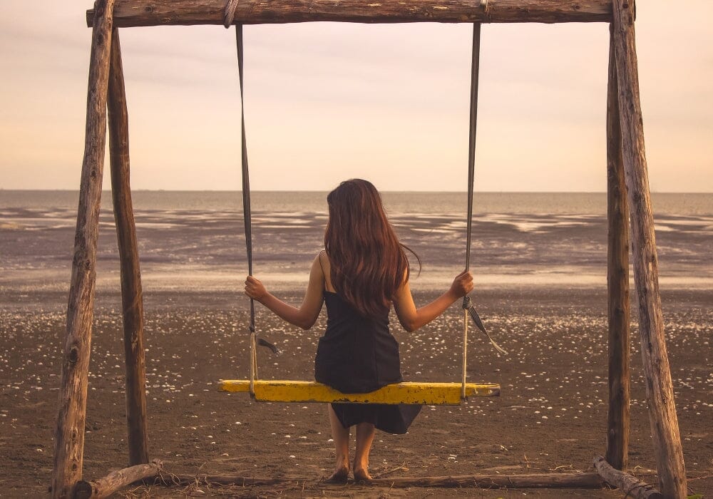 A woman sitting on a swing on a beach looking at the sea