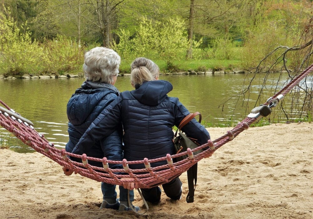 Two women sitting on a hammock by a river